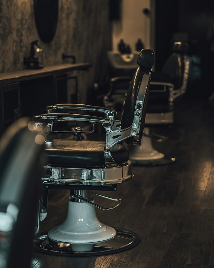 A chrome-framed barber chair on a dark hardwood floor in low light